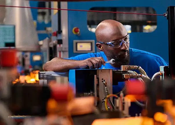 Eine Person arbeitet konzentriert an einer Maschine in einer industriellen Produktionsumgebung und überprüft Bauteile oder Einstellungen.