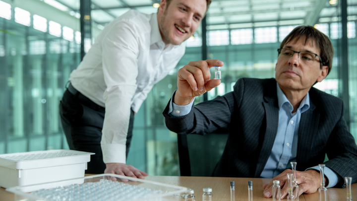 two men looking at a glass vial