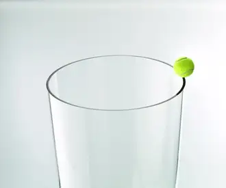 Yellow tennis ball balanced on the rim of a clear glass tube