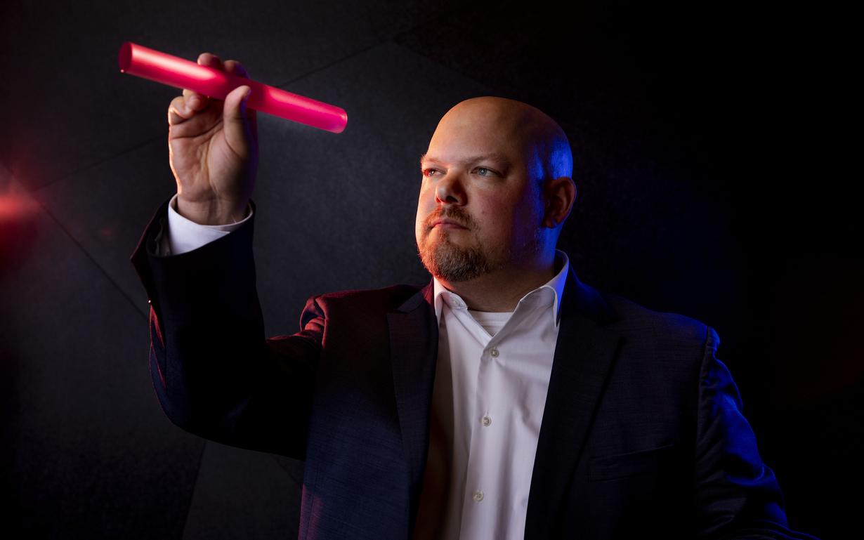 A man in business attire looking at a pink laser glass wand in his hand.