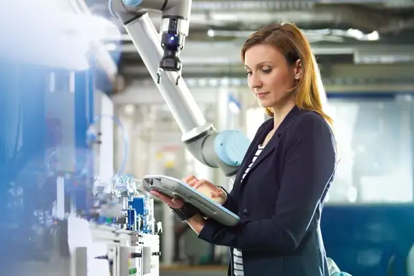 Eine Person bedient mithilfe eines Tablets eine automatisierte Maschine mit robotergestütztem Greifarm in einer Produktionsumgebung.