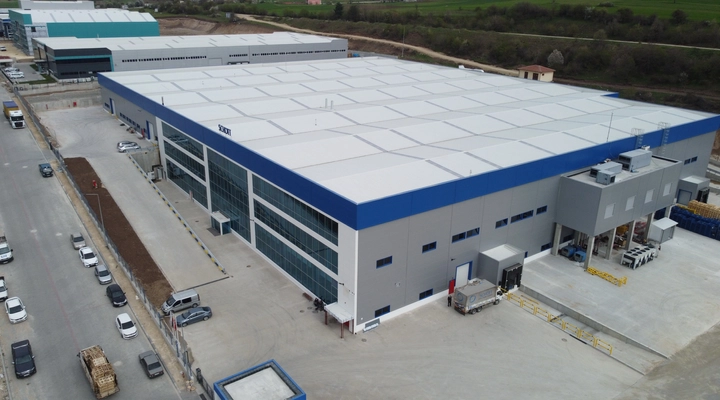 Modern industrial building with blue accents, large flat roof, and multiple loading docks, and adjacent warehouses.