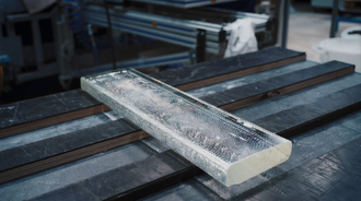 A block of clear, cool raw glass continues along the processing line