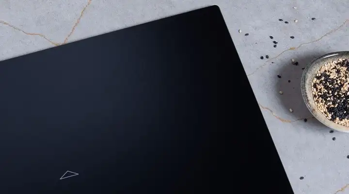 Black matte SCHOTT CERAN® cooktop surface on a light stone countertop, with a small bowl of black and white sesame seeds beside it.