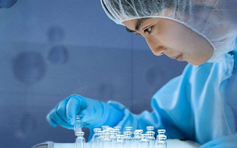 Woman in cleanroom clothing checks pharmaceutical vial