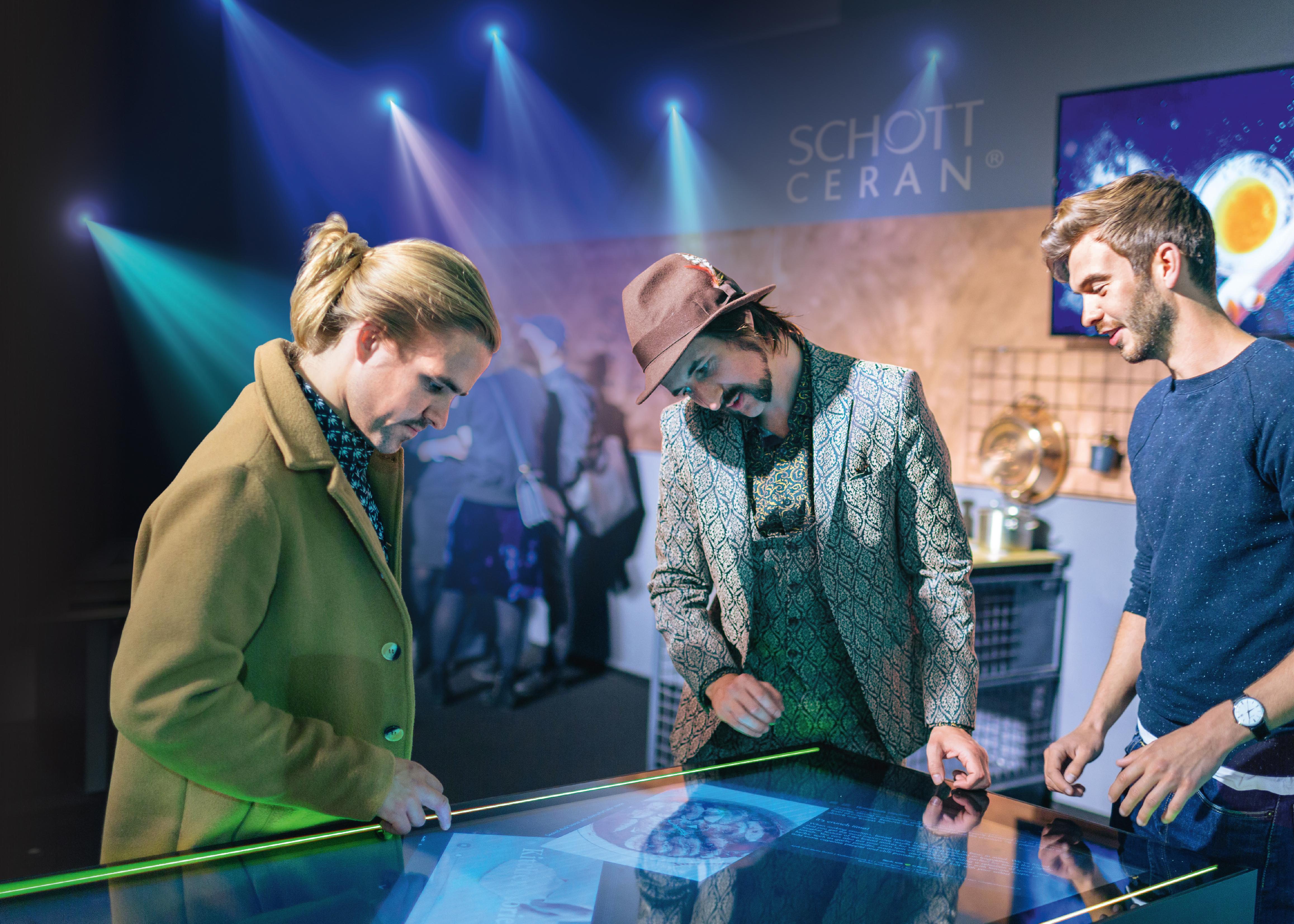  Eine Gruppe junger Leute betrachtet eine SCHOTT CERAN EXCITE® Glaskeramik-Kochfläche auf einer Ausstellung Zwei SCHOTT Qualitätsingenieure prüfen eine SCHOTT CERAN® Glaskeramik-Kochfläche