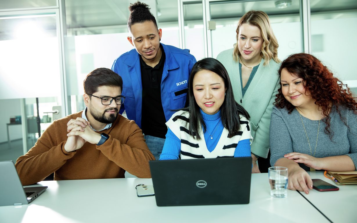 Three women and two men in front of a laptop.