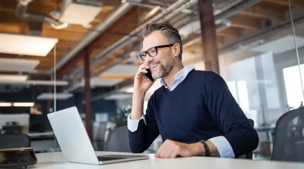 Man in glasses in business office on phone while working on laptop