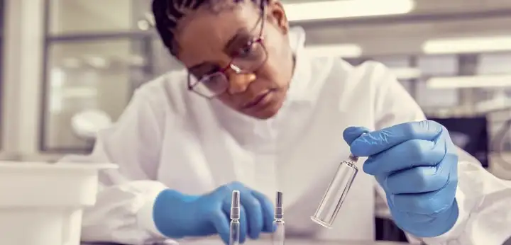 Scientist in gloves and lab coat examining syringe components at a laboratory bench