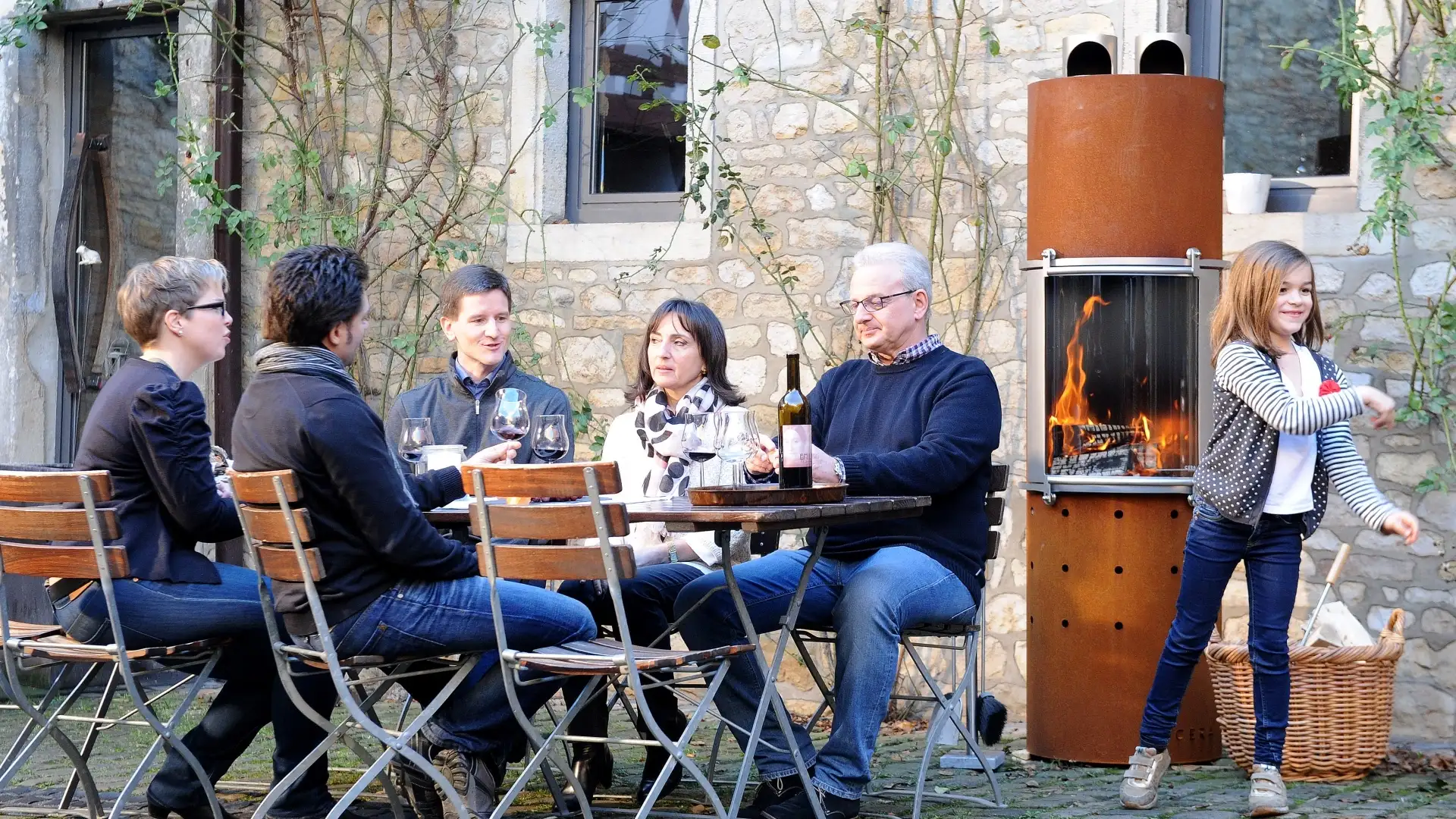 Familie sitzt an einem Outdoor-Tisch mit Kamin