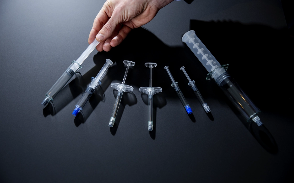 Seven different prefillable polymer syringes on a dark background.