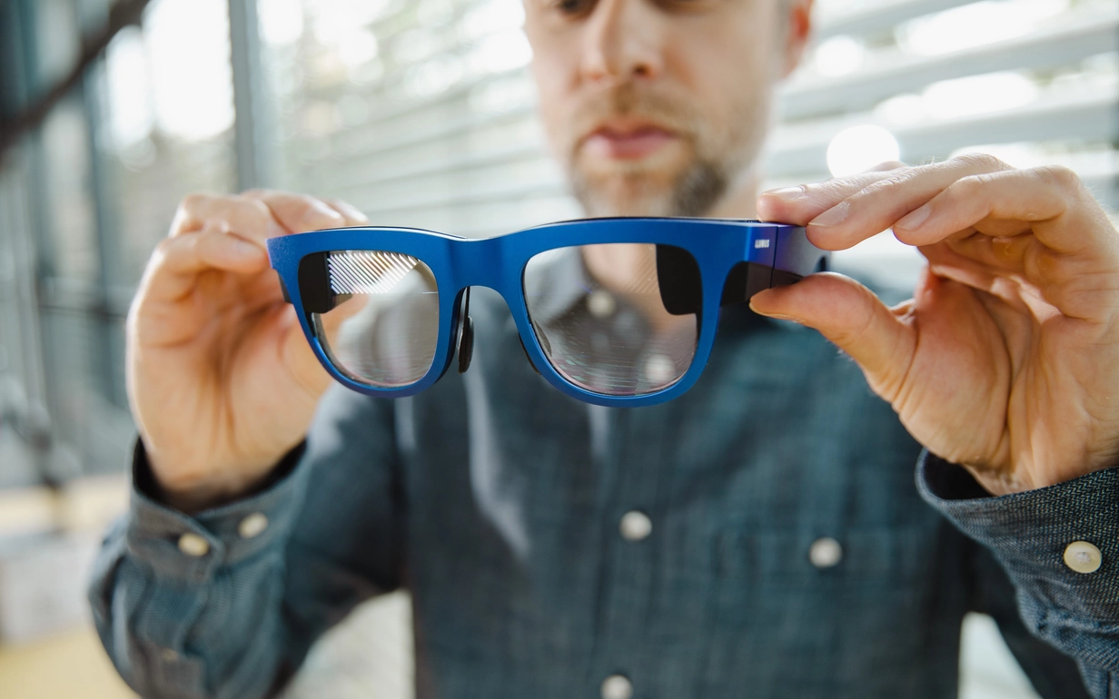 Man holding AR smart glasses with geometric reflective waveguides.