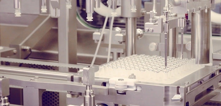 Automated pharmaceutical fill-finish machine dispensing liquid into a tray of small vials