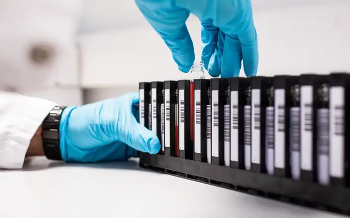 Gloved hands load glass packaging into a diagnostics container