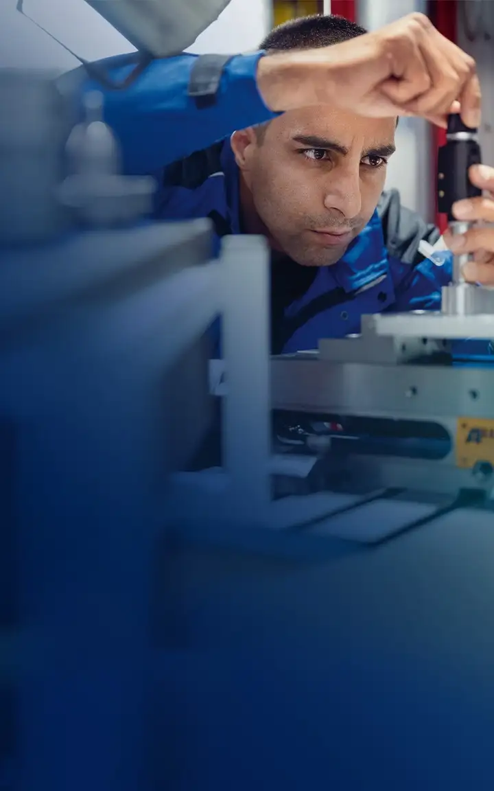 Fokussierte Person mit Produktions-Klamotten arbeitet an einem optischen Bauteil