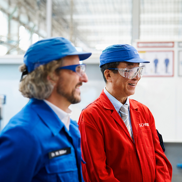 Zwei Personen in Arbeitskleidung stehen in einer Produktionshalle und unterhalten sich.