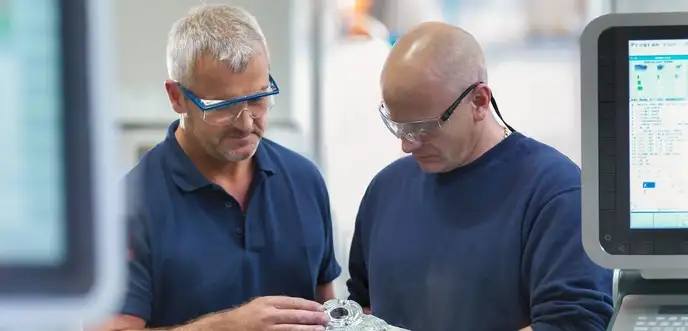 Dos ingenieros inspeccionan una pieza frente a un equipo de fabricación