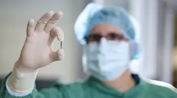 A doctor clad in surgical gowns holds Kitea's tiny sensor between his thumb and forefinger.