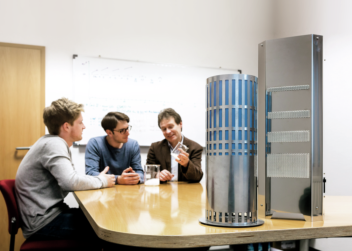 Tres hombres en una sala de reuniones de Triplan Umwelttechnik hablan sobre tubos de vidrio