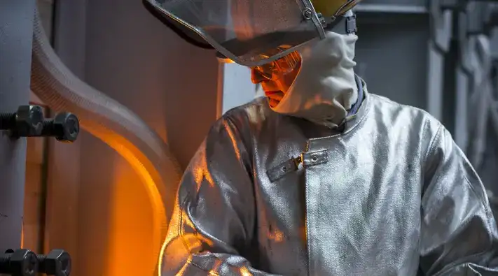 Man in a silver protective suit looks into the glass melt.