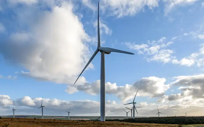 Ein großes Windrad im Vordergrund, viele Windräder im Hintergrund vor einem blauen Himmel mit großen Wolken