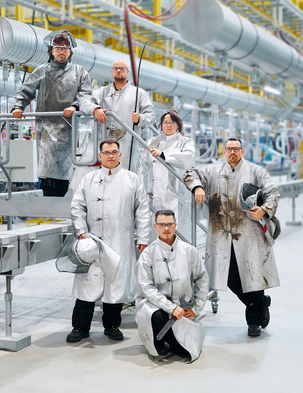 Sechs Personen in silberfarbener Schutzkleidung posieren in einer industriellen Produktionsanlage.