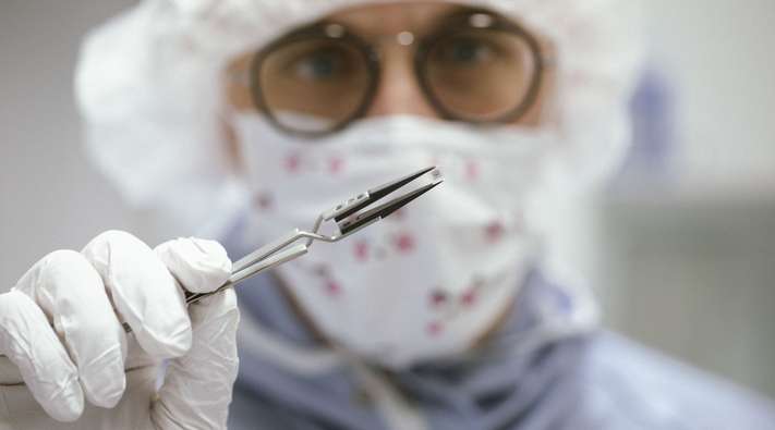 A laboratory employee who holds a miniaturized medical implant with tweezers