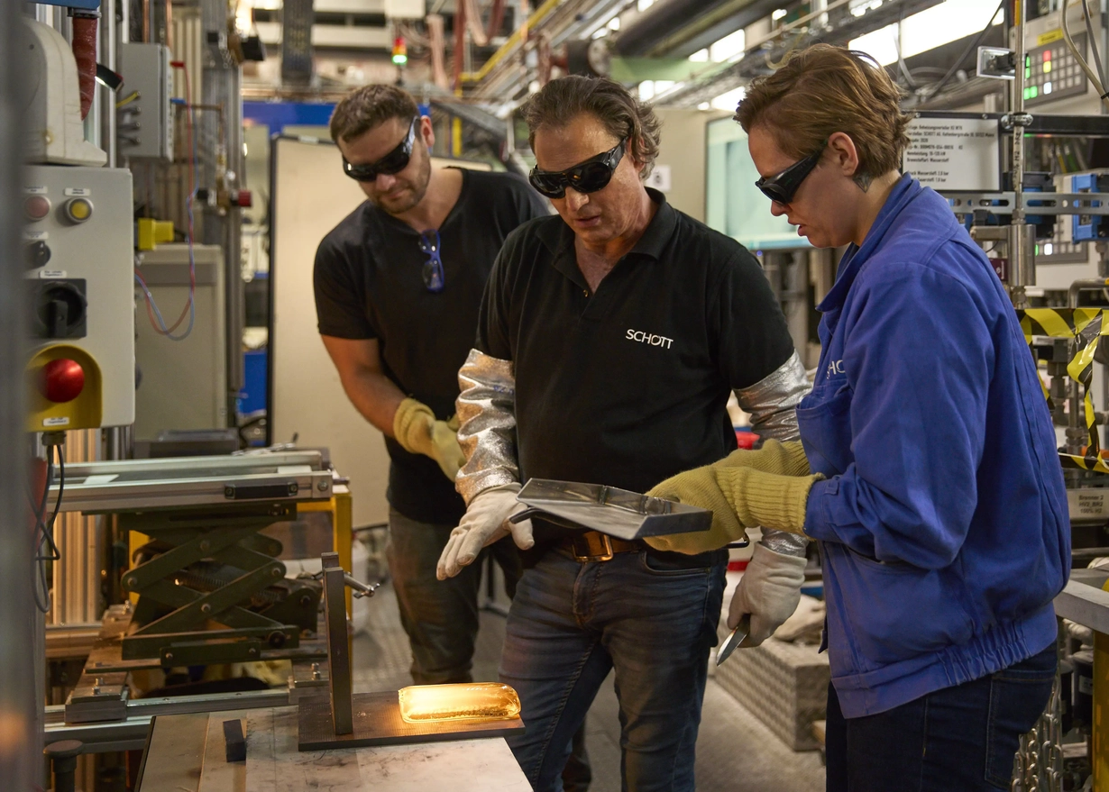 Zwei Männer und eine Frau in Arbeitskleidung mit Sicherheitsbrille an der Testschmelze.