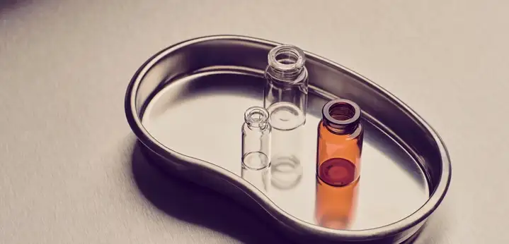 Three small glass vials, one amber and two clear, standing on a stainless steel tray