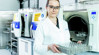 Female technician looks to camera holding a tray of glass vials