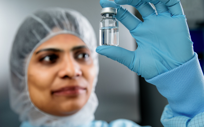 	Frau in Reinraumkleidung hält eine Ampulle in der Hand.