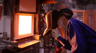 Glass technician with protective equipment looks into glass melting oven