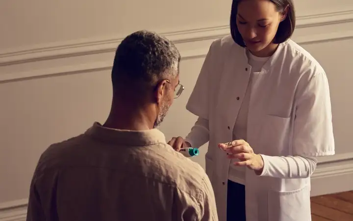 Healthcare professional examining a seated patient while holding a small medical device