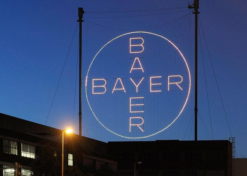 Leuchtreklame mit Bayer-Logo vor einer Produktionsstätte