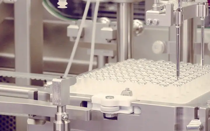 Automated pharmaceutical fill-finish machine dispensing liquid into a tray of small vials