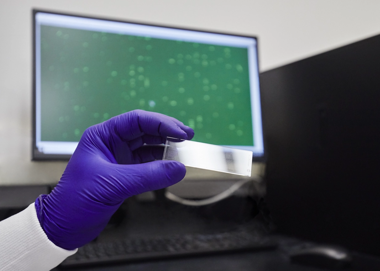 Gloved hand holding a glass slide in front on a computer monitor