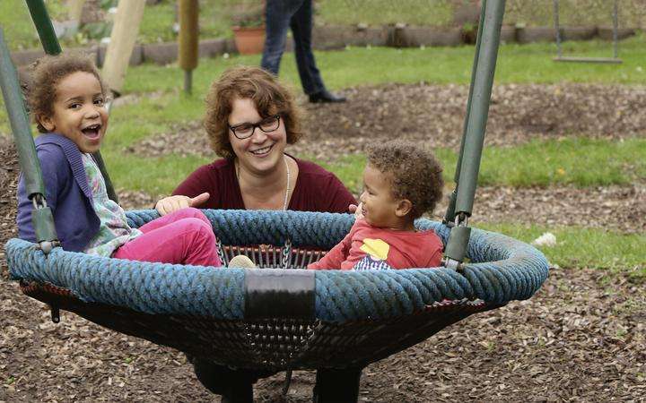 Woman playing with two children on swing