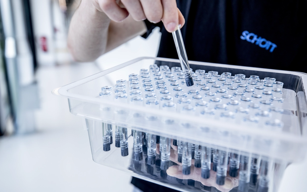 A SCHOTT employee holds a prefillable polymer syringe above a nest and tub.