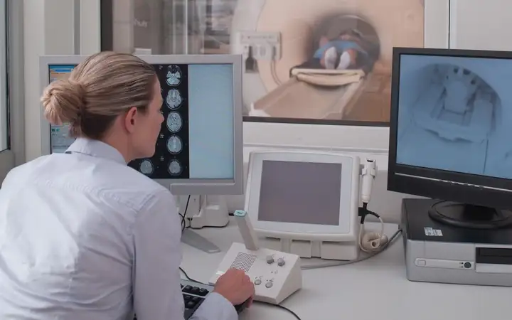 Female doctor looking at two displays while a patient is being examined in an MRI machine