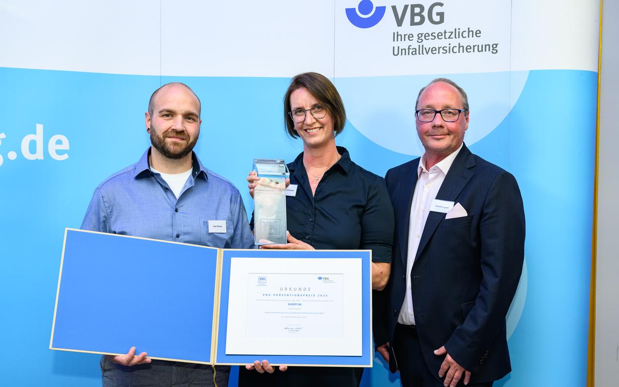 Eine Frau und zwei Männer von SCHOTT mit der Urkunde und dem Preis der VBG.