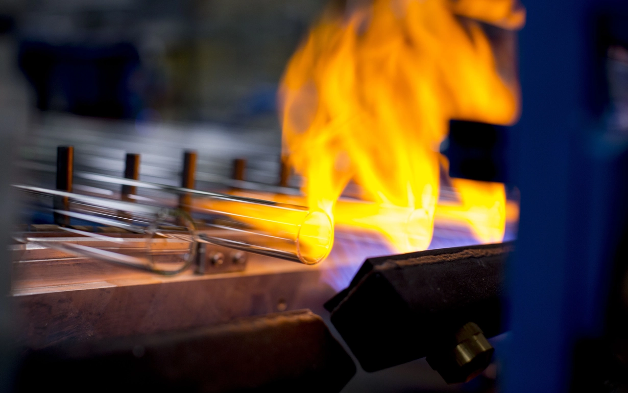Man with heat protective clothing looking into the glass melting tank