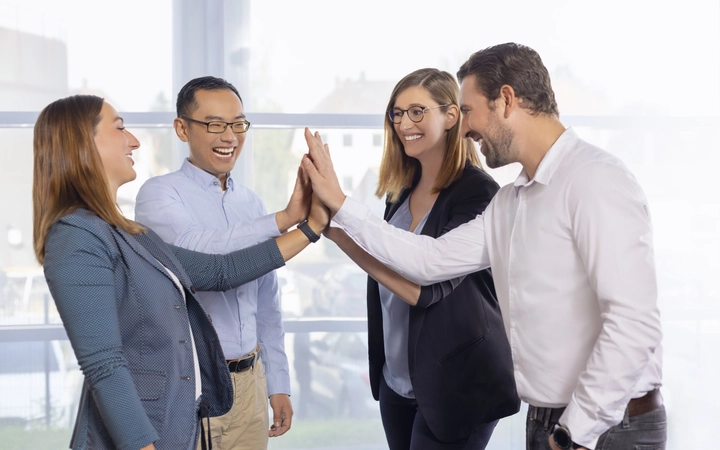 A group of four colleagues in a business environment smiling and giving a high-five