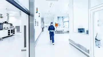 A woman in a protection suit walks through a lab.