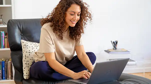 Eine Person sitzt entspannt auf einem Sessel und arbeitet an einem Laptop.