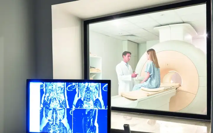 Male doctor talking to female patient sitting on MRI equipment in front of a display