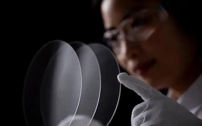 Woman wearing safety glasses inspects round glass panel.