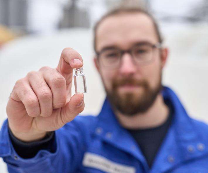 Marius Amschler stands in front of the SCHOTT cullet warehouse and holds a vial up to the camera