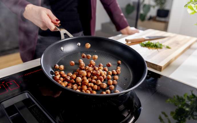 Woman swivels pan with nuts on CERAN® glass ceramic cooking surface