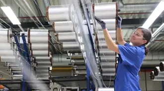 Woman in blue SCHOTT work clothes in the production of fiber optic conductors wound onto rolls.