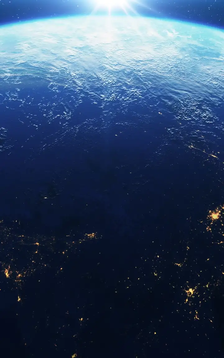 View of Earth from space at sunrise, with glowing city lights visible across continents under a starry sky
